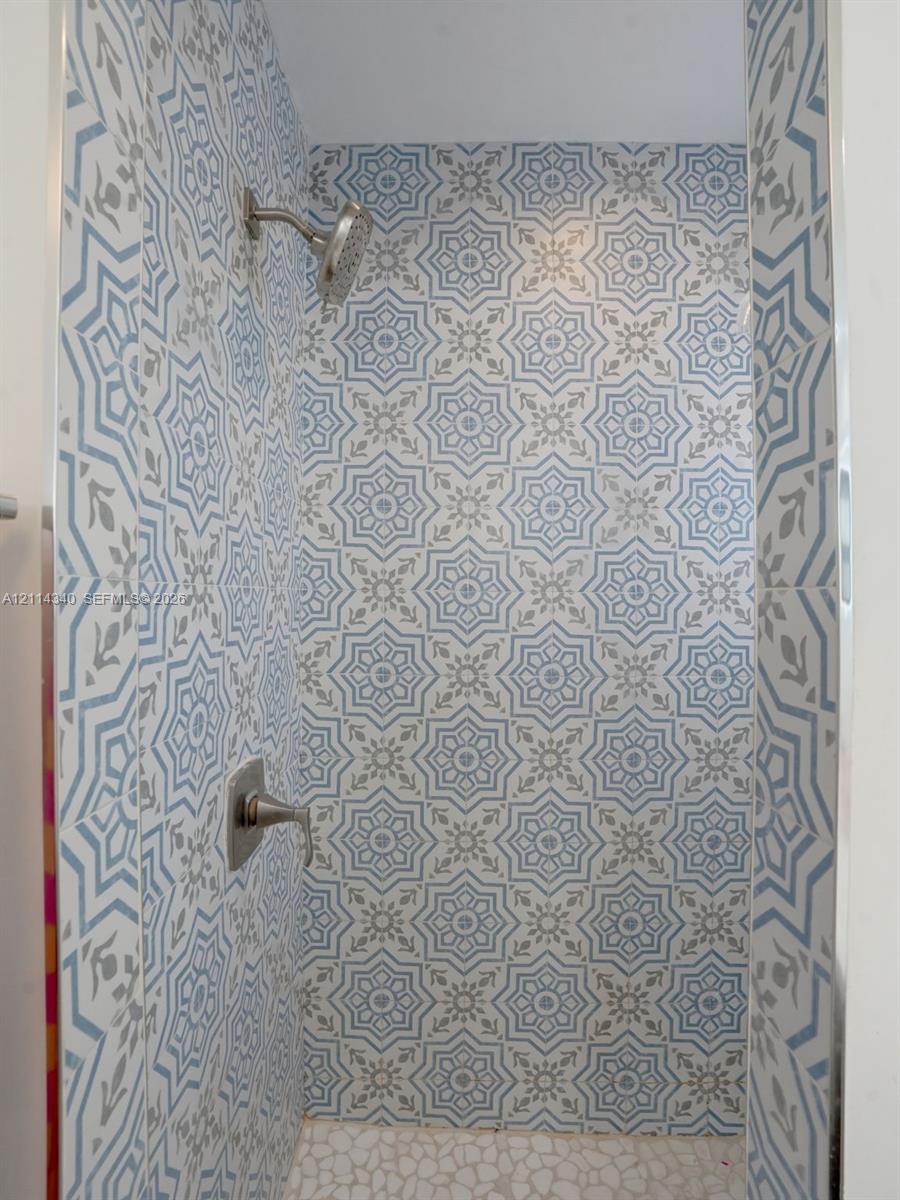 Shower stall featuring patterned blue and white tile wall accents, a pebble-finish floor, and brushed-finish plumbing fixtures