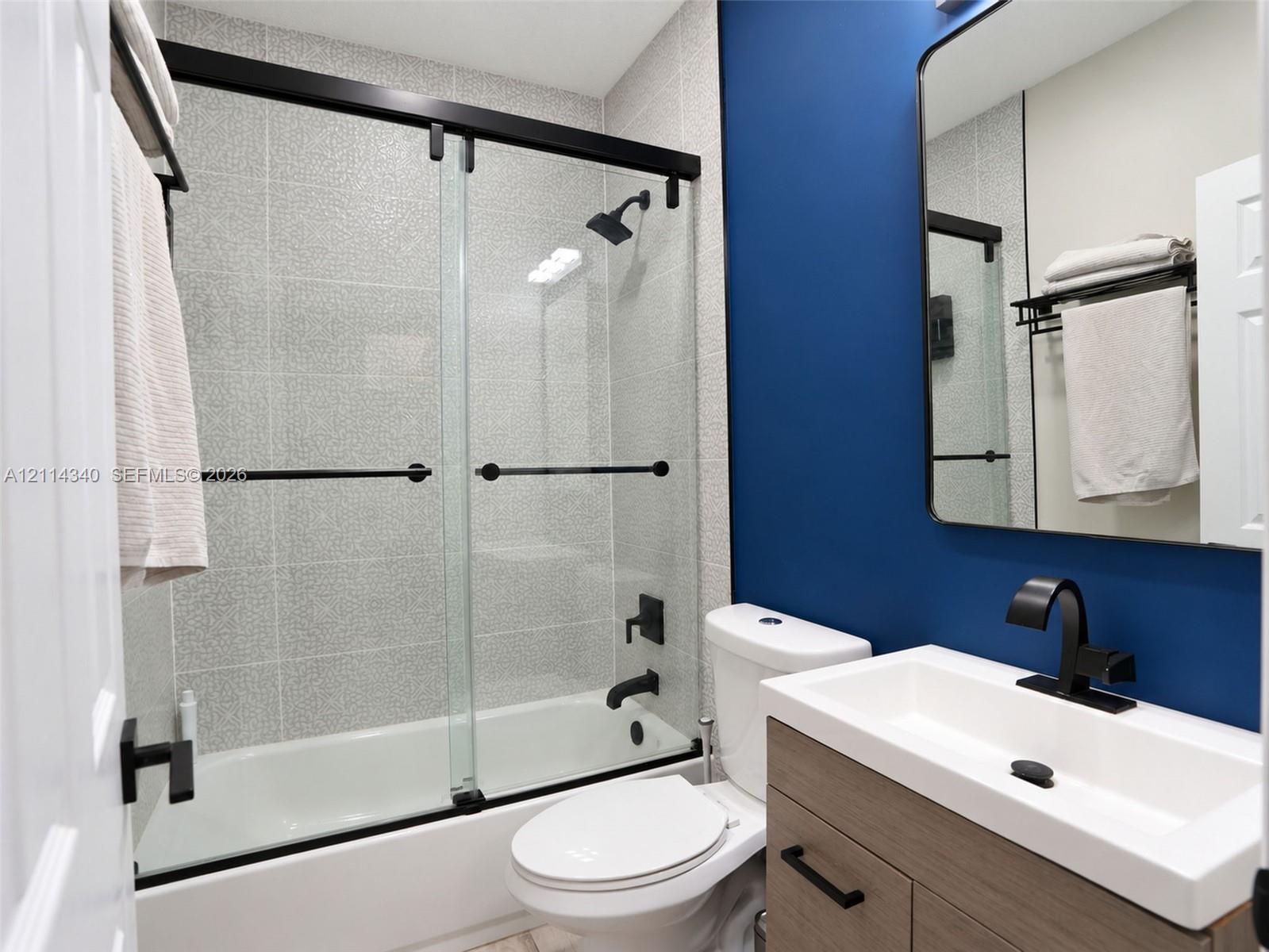 Bathroom featuring a wood-finish vanity with a rectangular basin, matte black fixtures, a glass shower enclosure with sliding doors, and tiled shower surround