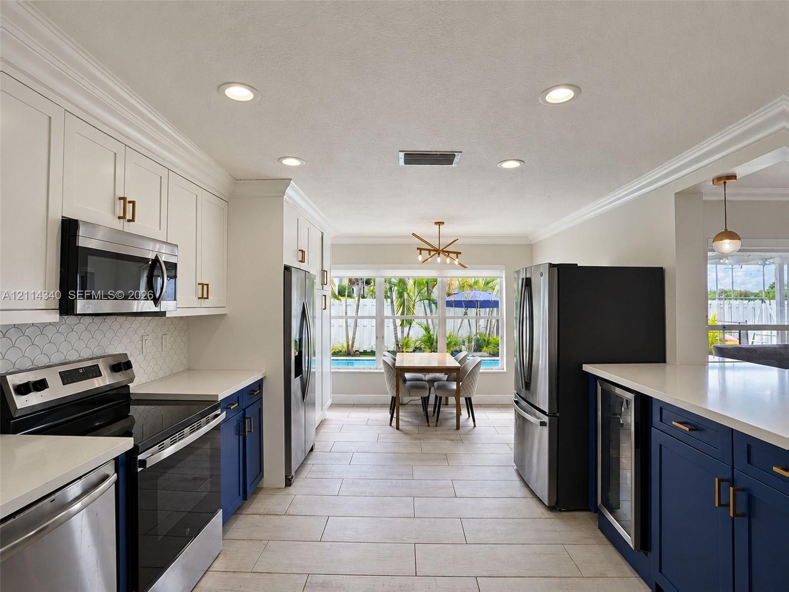 Kitchen featuring white upper cabinetry, navy blue lower cabinetry, stainless steel appliances, quartz countertops, and scalloped tile backsplash