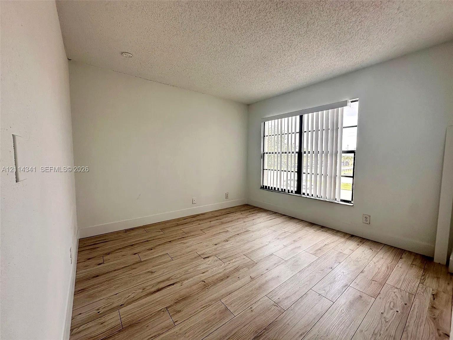 Room featuring wood-finish flooring, a multi-pane window with vertical blinds, and a textured ceiling