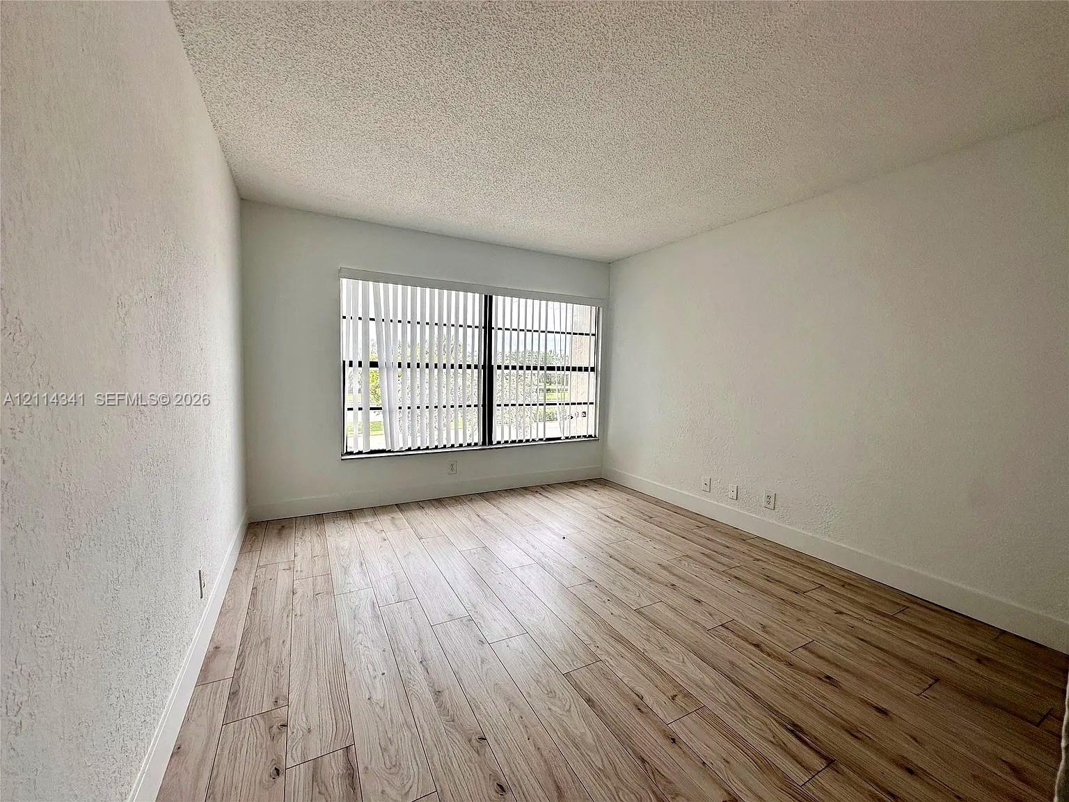 Interior space featuring wood-finish flooring, white walls, and a large window with vertical blinds Interior space featuring wood-finish flooring, white walls, and a large window with vertical blinds