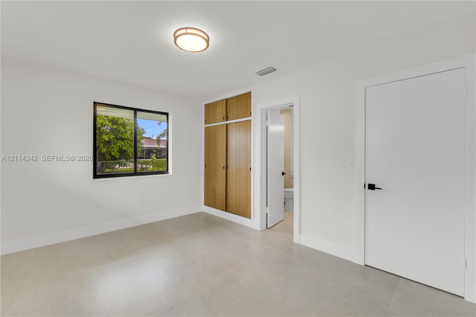 Room featuring neutral tile flooring, built-in floor-to-ceiling wood-finish cabinetry, a flush-mount circular light fixture, and black door hardware