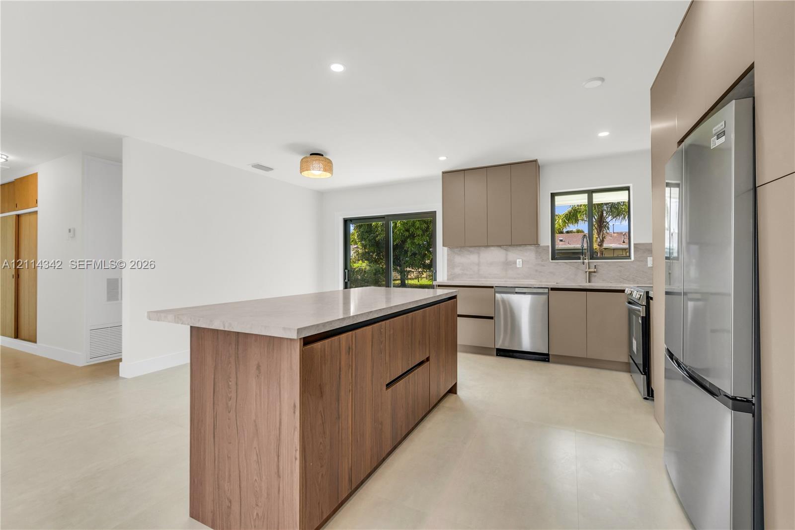Kitchen featuring a wood-finish island, solid-surface countertops, flat-panel cabinetry, stainless steel appliances, and recessed lighting
