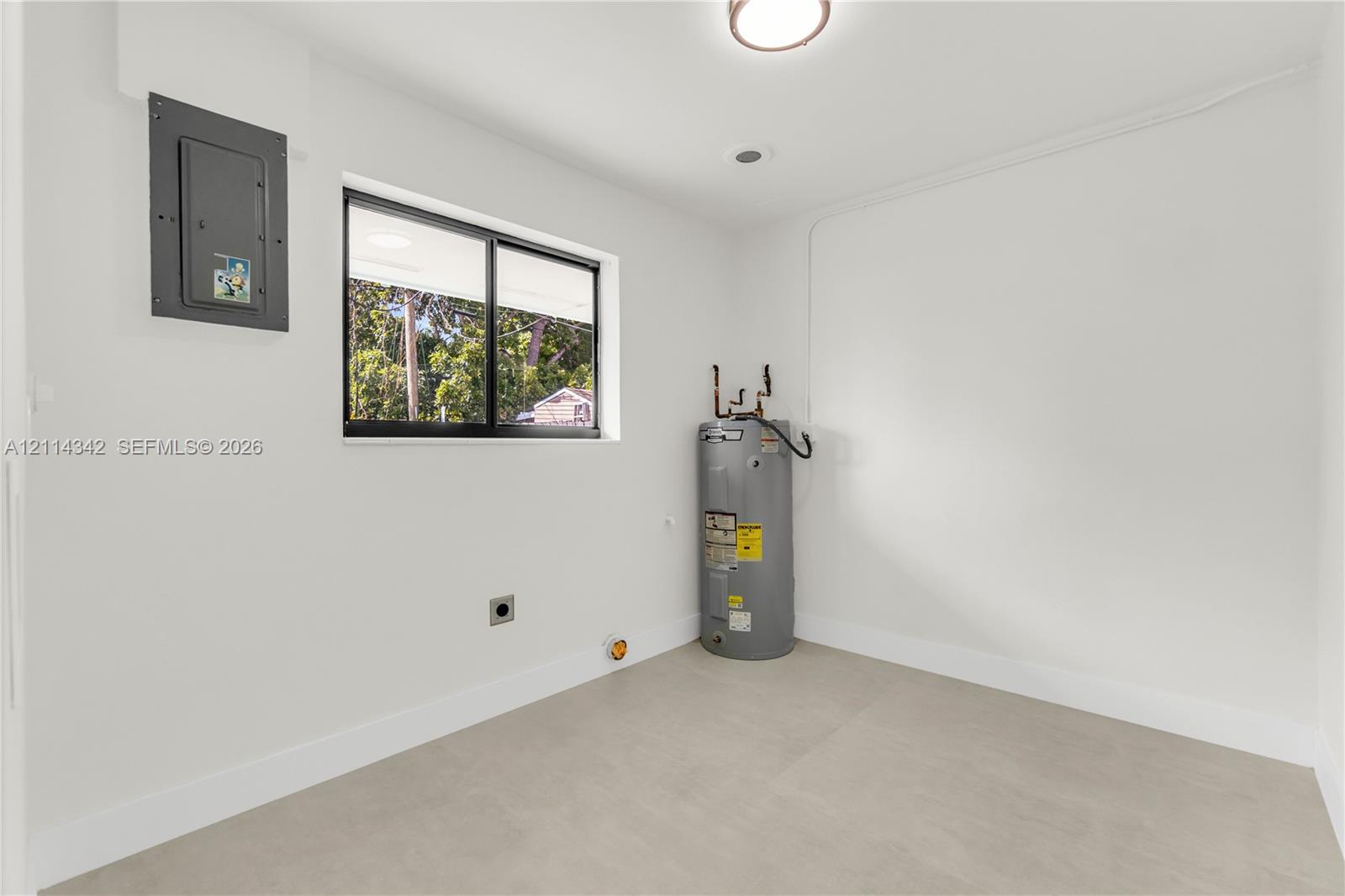 Utility space featuring neutral-toned tile flooring, a mounted electrical panel, a sliding window, and a vertical water heater