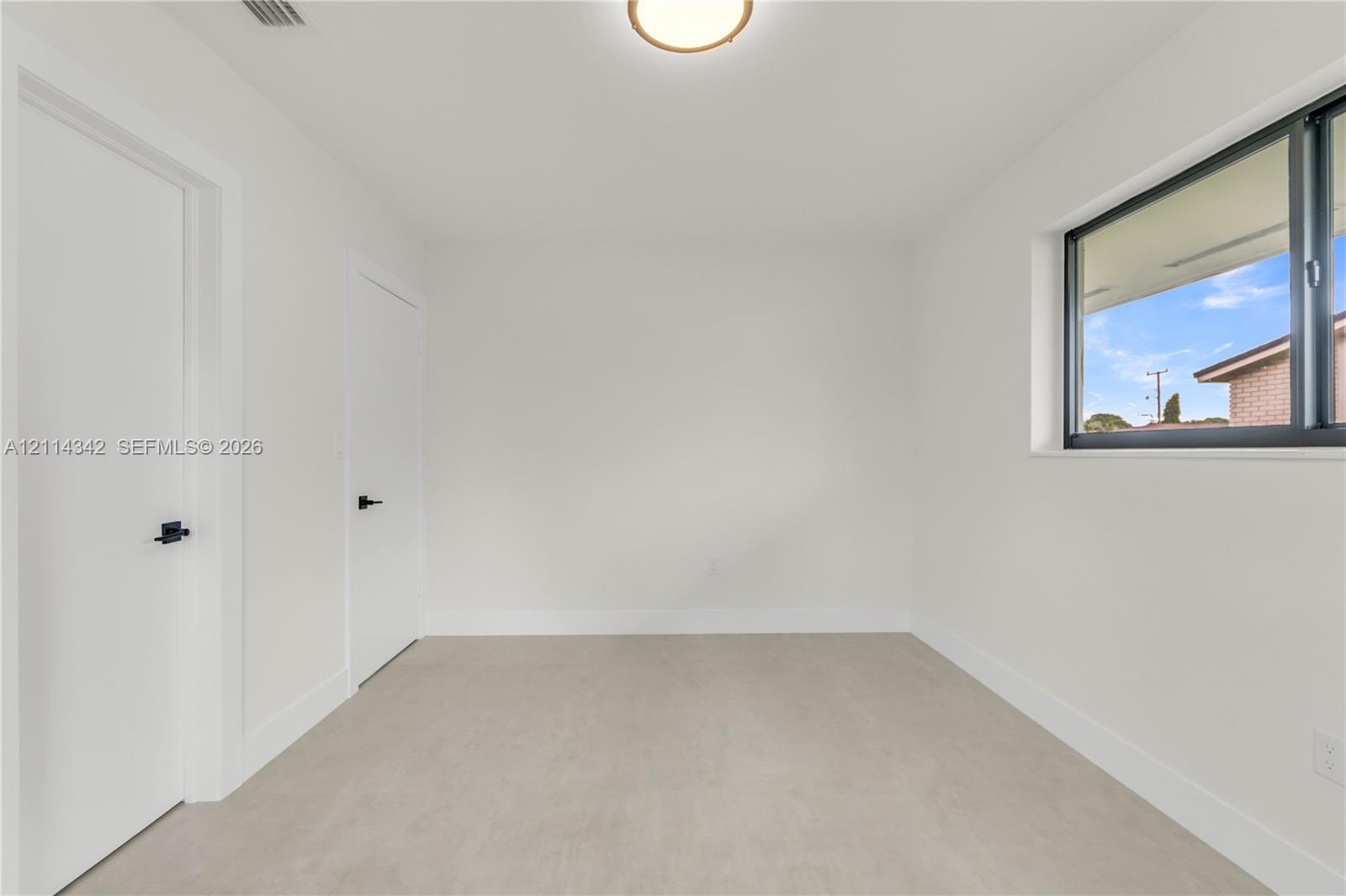 Bright interior featuring neutral-toned flooring, two doors with matte black hardware, a flush-mount ceiling light, and a window with a dark frame
