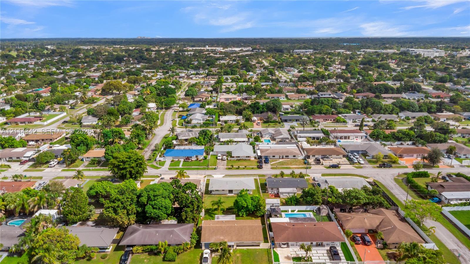 Aerial perspective of a suburban neighborhood featuring single-story residential dwellings, concrete street grids, established trees, and private swimming pools