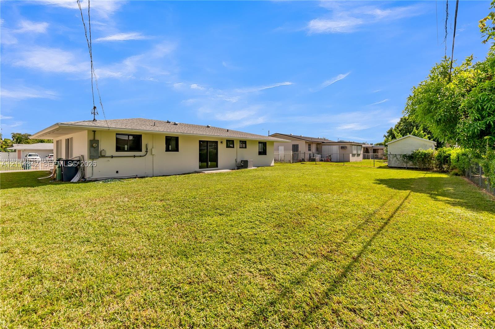 Expansive backyard featuring a large grass lawn, a detached storage structure, and perimeter fencing