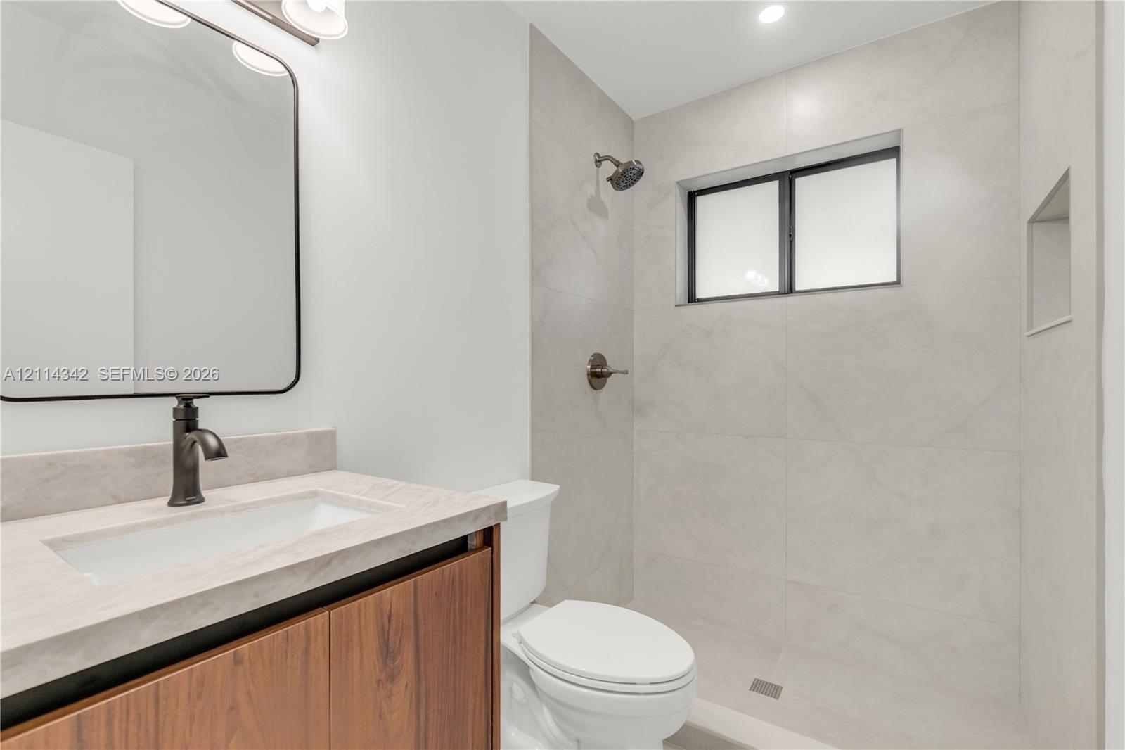 Bathroom featuring a wood-finish vanity, rectangular vessel sink, stone-finish countertop, walk-in shower with tile surround, and built-in recessed niche