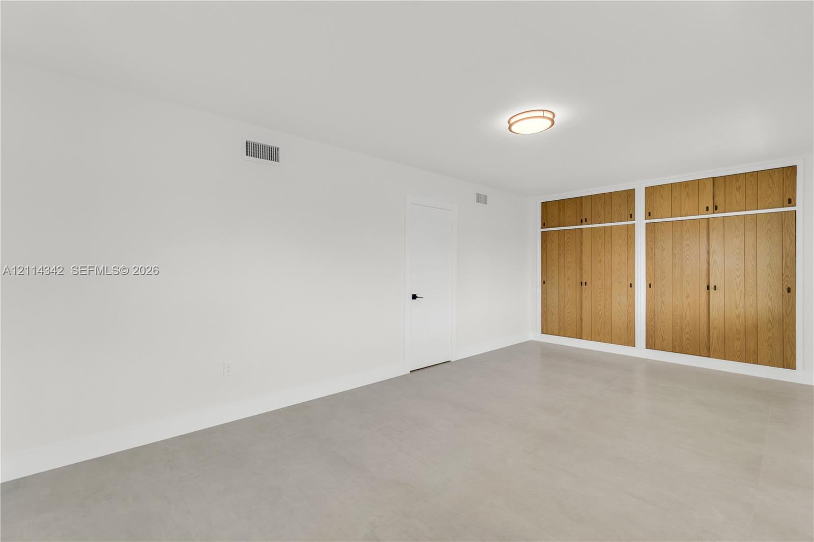 Neutral-toned flooring, expansive wall-to-wall built-in wood cabinetry, and a flush-mount circular ceiling fixture