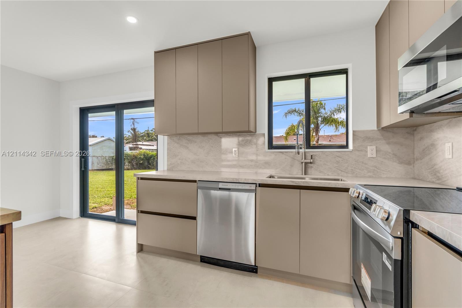 Kitchen featuring flat-panel cabinetry, full-height stone-finish backsplash, stainless steel appliances, and large-format tile flooring with access to the exterior via sliding glass doors