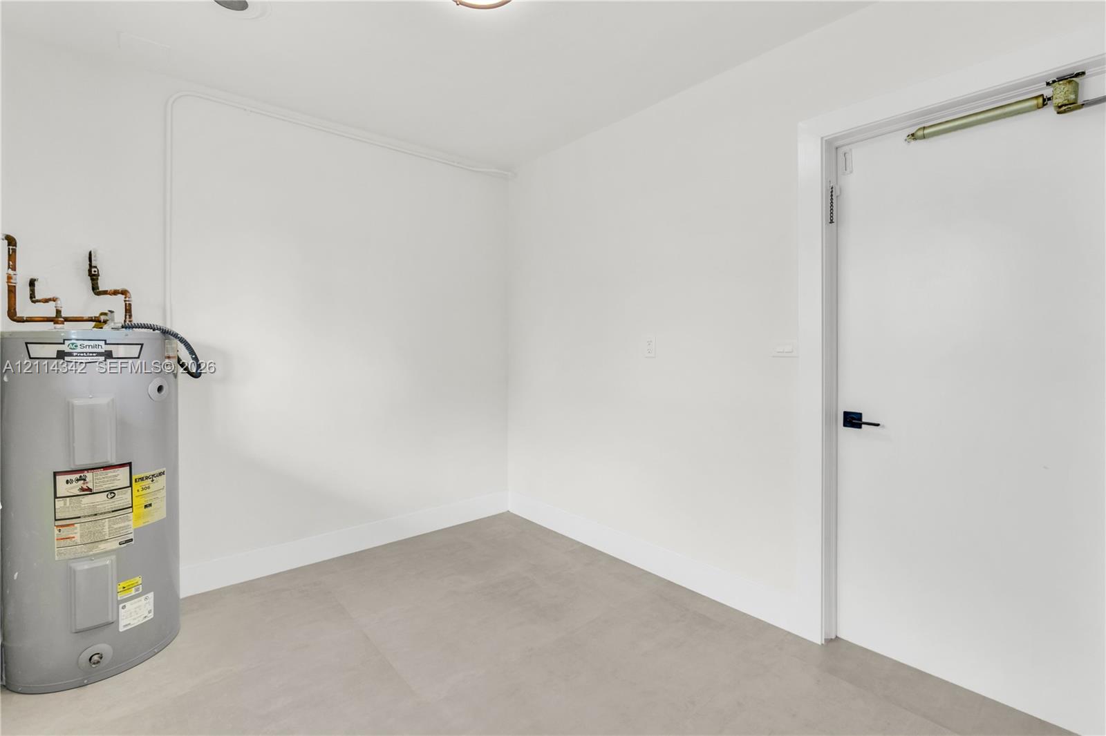 Utility space featuring an upright water heater, smooth-finish flooring, and a door with a heavy-duty hydraulic closer
