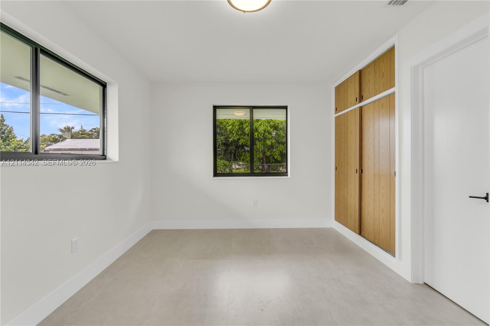 Room featuring large windows with black frames, tile flooring, and integrated wood-finish cabinetry