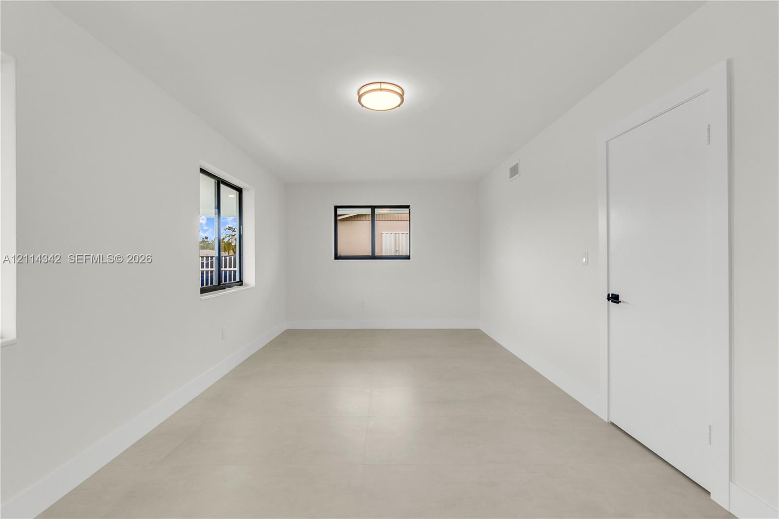 Interior room featuring neutral wall finishes, large-format tile flooring, black-framed windows, and a flush-mount circular ceiling fixture