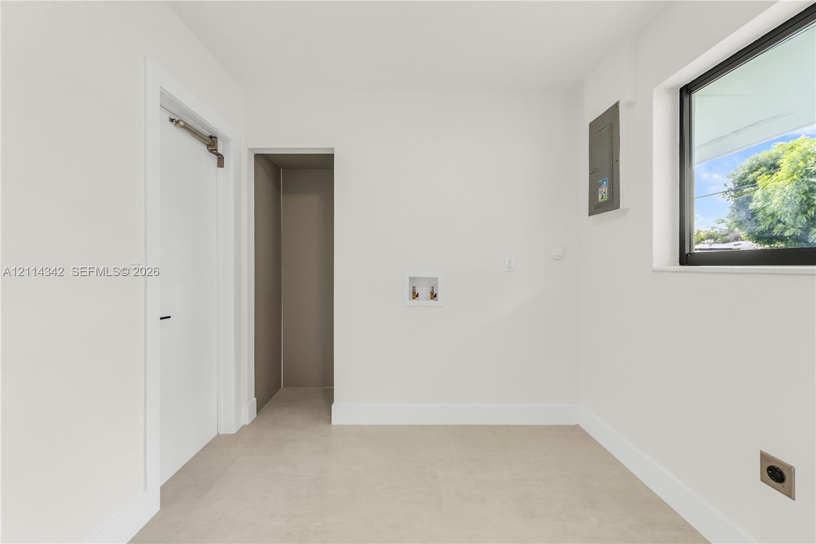 Utility room featuring neutral tile flooring, a window with a black frame, recessed doorway, and dedicated water hookups