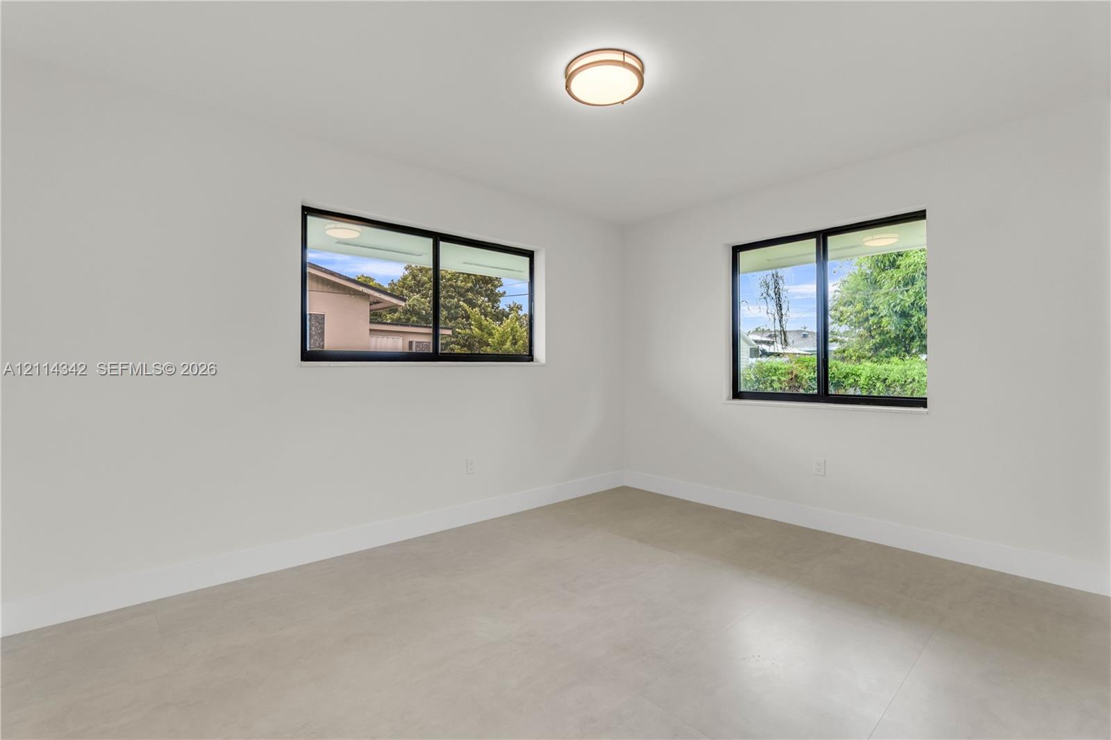 Neutral-toned tile flooring, dual windows with black frames, and a contemporary flush-mount ceiling light fixture