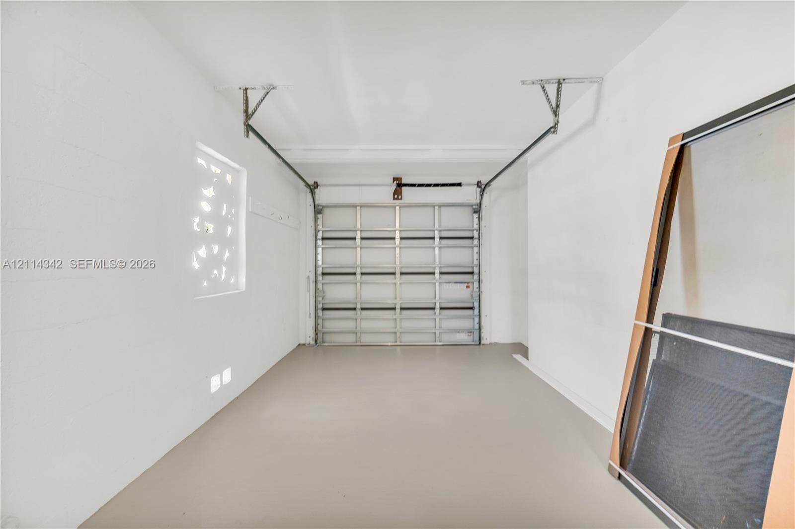 Enclosed garage featuring finished concrete flooring, painted masonry walls, a metal sectional door, and an integrated glass block window