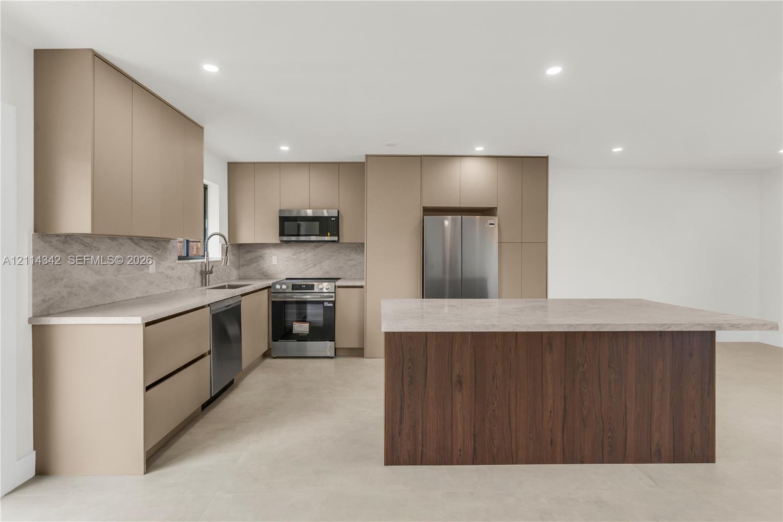 Kitchen featuring flat-panel cabinetry, stone-surface countertops, full-height stone backsplash, wood-finish center island, and stainless steel appliances