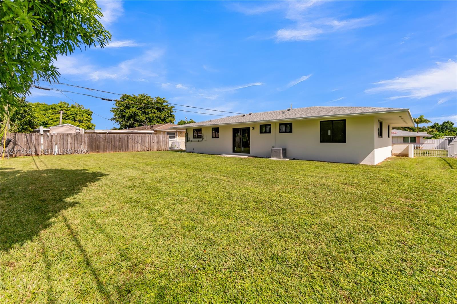 Expansive backyard featuring a large grass lawn, perimeter wood fencing, and exterior stucco siding