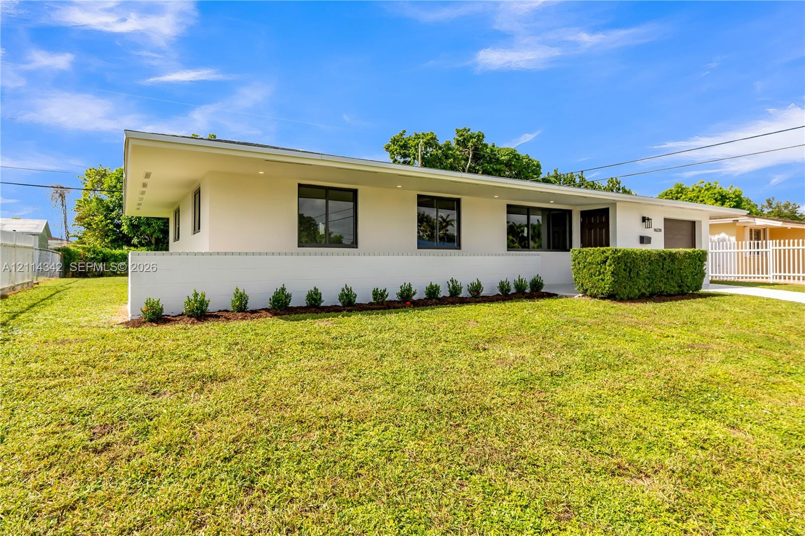 Mid-century modern exterior featuring a low-slope roof, crisp white stucco finish, recessed soffit lighting, and manicured foundation plantings