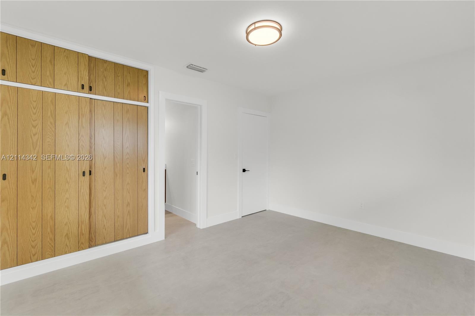 Built-in wood-finish cabinetry, neutral flooring, white interior doors with matte black hardware, and a flush-mount circular ceiling light fixture