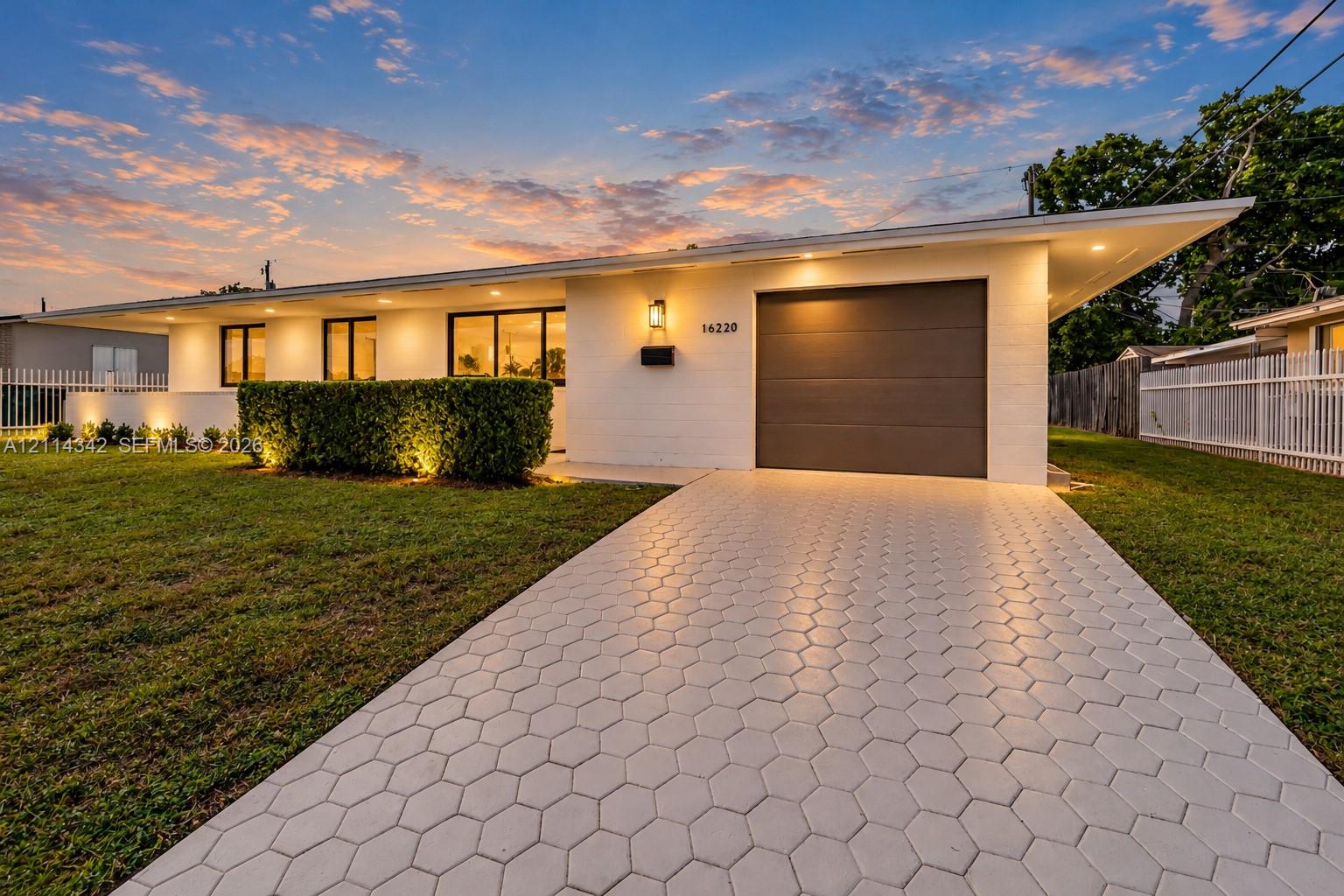 Mid-century modern exterior featuring painted brick masonry, an attached garage, geometric paver driveway, and recessed roofline lighting
