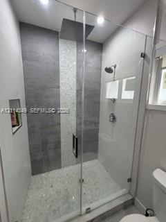 Walk-in shower featuring a frameless glass enclosure, ceiling-mounted rainfall showerhead, pebble stone floor, vertical mosaic tile accent, and a built-in recessed wall niche
