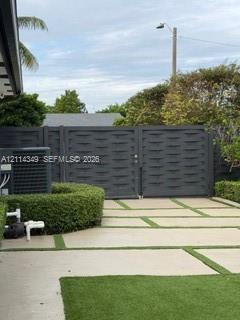 Private driveway featuring concrete pavers with artificial turf inlay, enclosed by a charcoal-finished privacy gate and manicured perimeter hedges