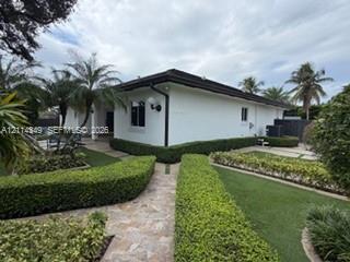 Single-story exterior featuring white stucco finish, dark-toned hip roof, stone-paver walkways, and manicured shrubbery