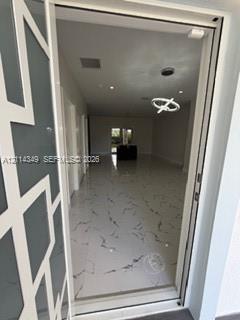 Entryway featuring a glass door with a geometric overlay, large-format tile flooring with veining detail, recessed ceiling lighting, and a modern sculptural pendant fixture Entryway featuring a glass door with a geometric overlay, large-format tile flooring with veining detail, recessed ceiling lighting, and a modern sculptural pendant fixture
