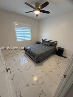 Large-format tile flooring with veined detailing, neutral wall tones, multi-blade ceiling fan with integrated lighting, and horizontal shade window treatment