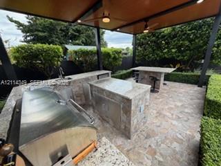 Covered outdoor kitchen featuring stone-clad islands, integrated stainless steel grill, stone-finish countertops, built-in sink, and ceiling fans