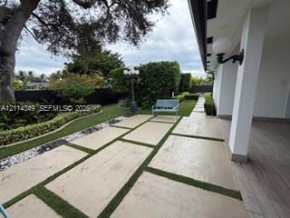 Covered patio featuring wood-finish flooring, large-format concrete pavers with turf inlays, professional landscaping, and wall-mounted exterior lighting