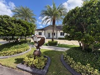 Exterior facade featuring a paved driveway, manicured landscaping, stone garden borders, and mature palm trees Exterior facade featuring a paved driveway, manicured landscaping, stone garden borders, and mature palm trees