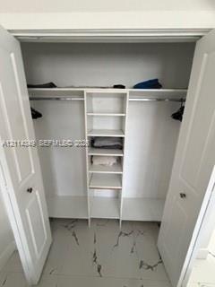 Walk-in closet featuring white-finish built-in shelving, two overhead storage ledges, metal hanging rods, and large-format tile flooring with a veined pattern