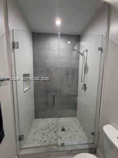 Walk-in shower featuring a glass enclosure, gray tile surround, pebble-style floor, built-in recessed niche, and handheld shower fixture