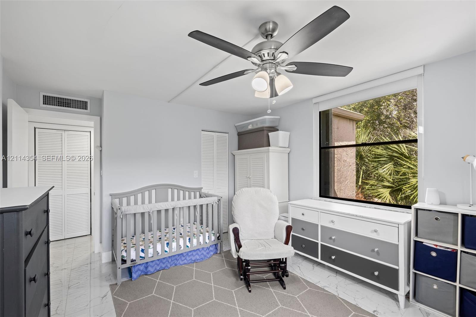 Room featuring large-format tile flooring, a multi-blade ceiling fan with integrated lighting, and louvered closet doors