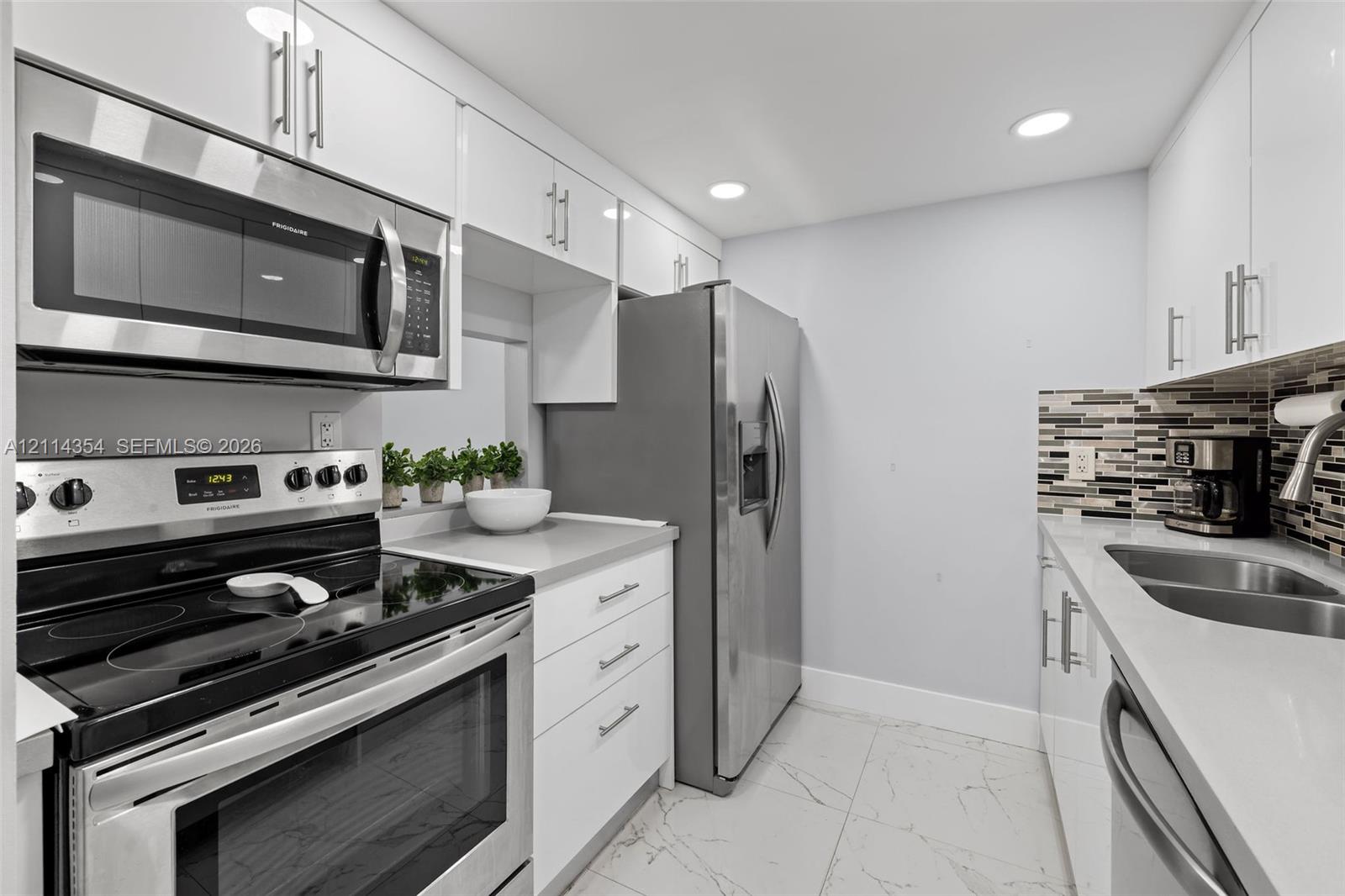 Kitchen featuring white gloss cabinetry, stone-finish countertops, stainless steel appliances, a multi-tone glass tile backsplash, and large-format porcelain tile flooring