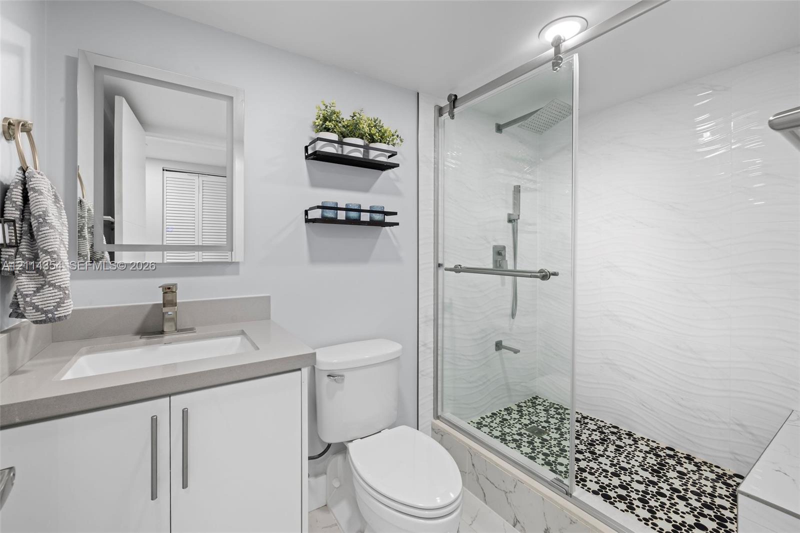 Bathroom featuring a vanity with a solid-surface countertop, walk-in shower with sliding glass doors, textured wall tile, and stone-tiled shower floor
