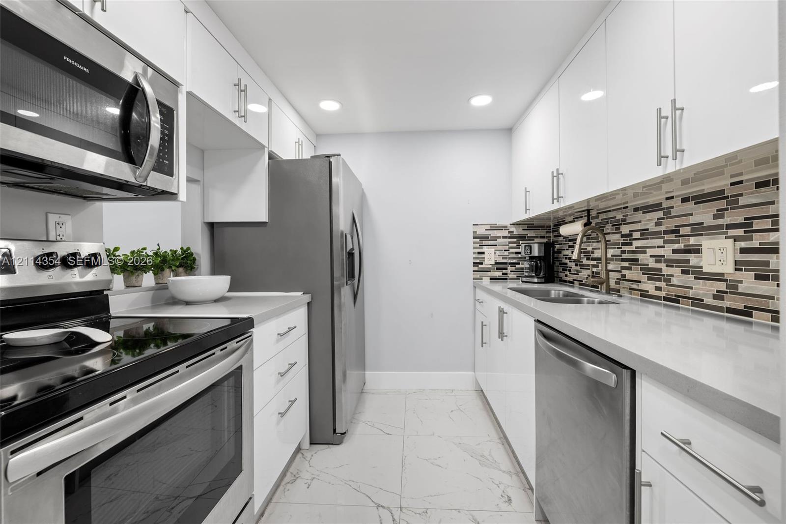 Kitchen featuring white high-gloss cabinetry, stainless steel appliances, multi-tonal linear tile backsplash, solid-surface countertops, and large-format tile flooring