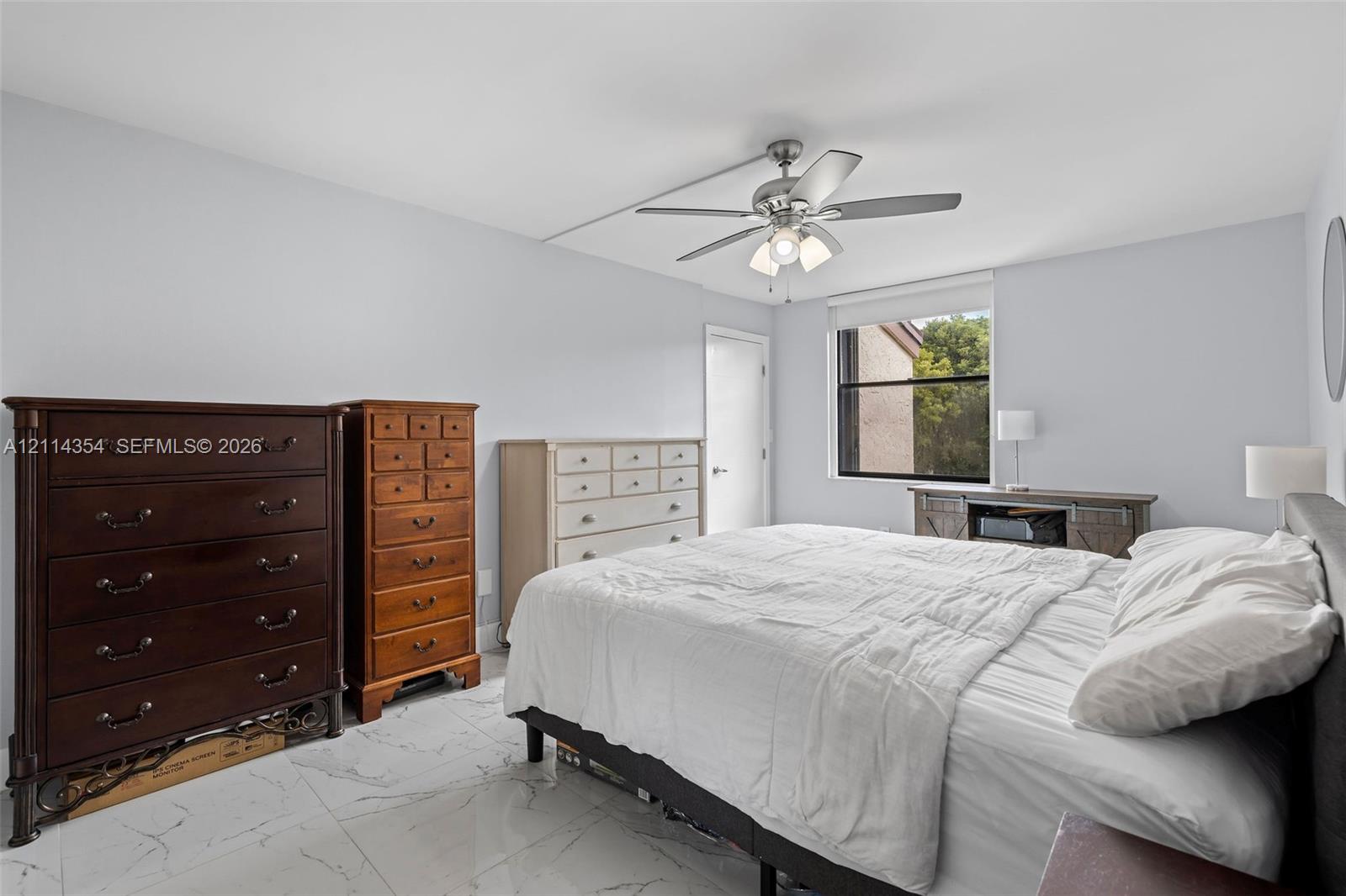 Neutral-toned room featuring large-format stone-finish tile flooring, a multi-blade ceiling fan with an integrated light fixture, and a single-pane window