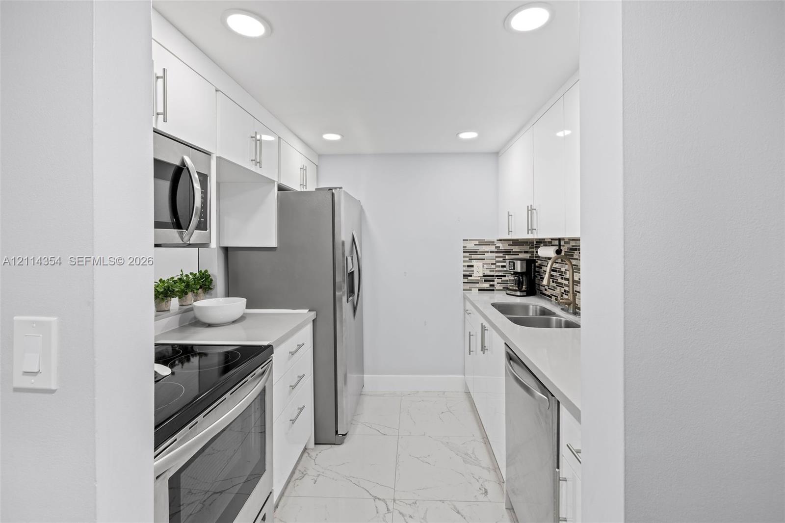 Kitchen featuring white high-gloss cabinetry, stainless steel appliances, quartz countertops, a multi-tone tile backsplash, and large-format tiled flooring