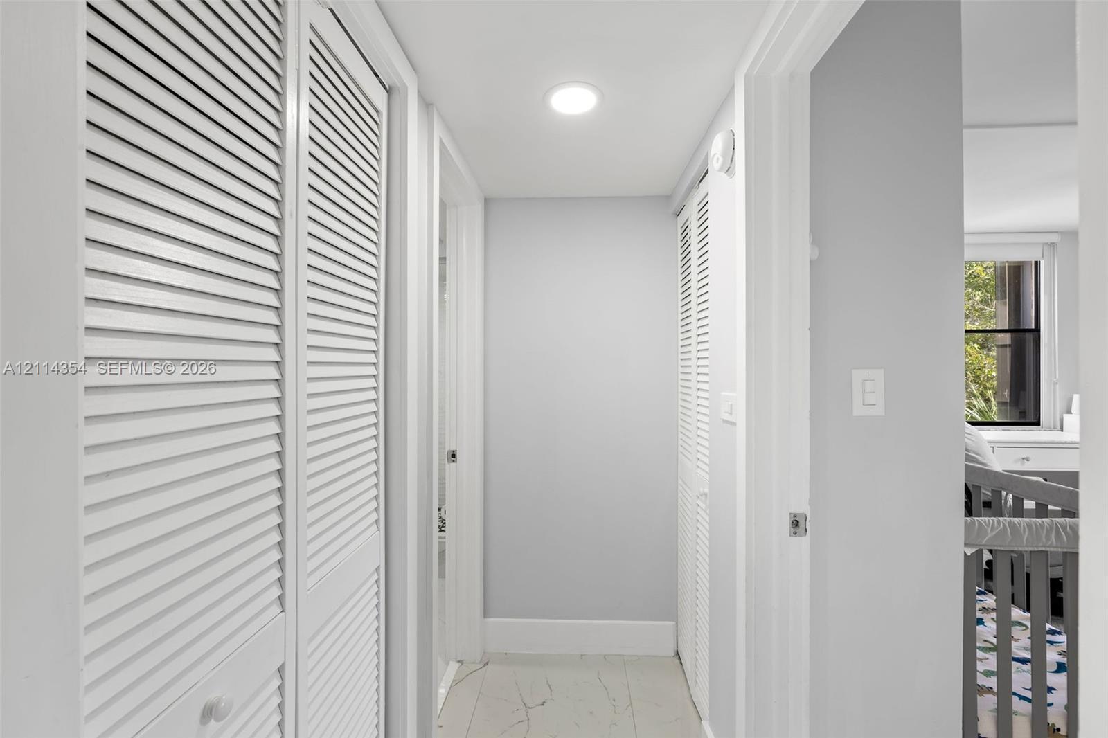 Hallway featuring white louvered-style closet doors, recessed ceiling lighting, and tile flooring