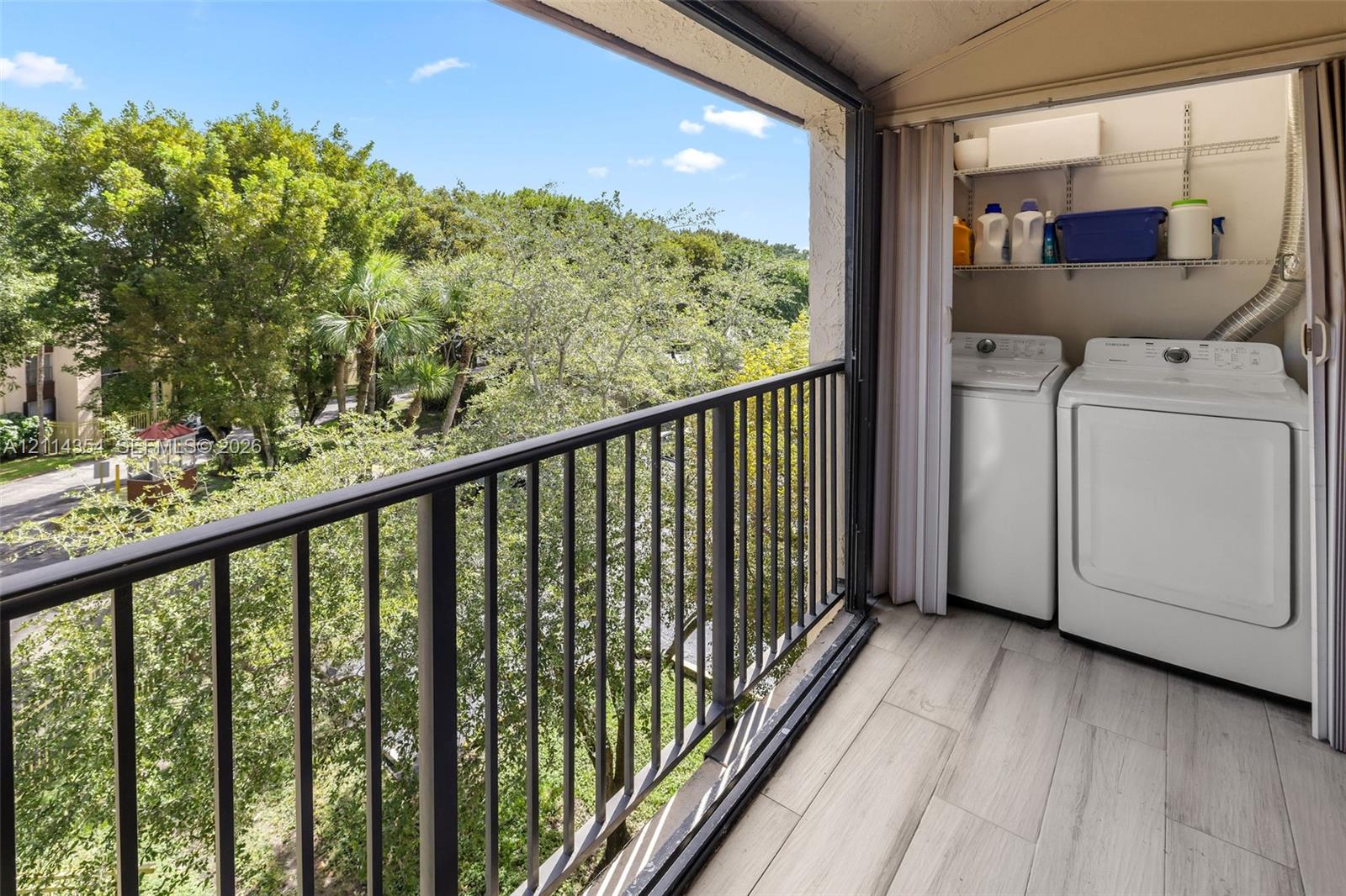 Balcony featuring black metal railing, wood-finish tile flooring, and integrated laundry area with wire shelving