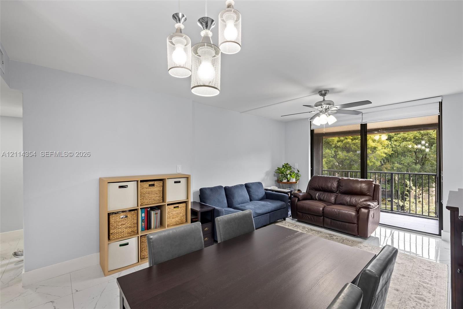 Open-concept interior featuring large-format polished tile flooring, industrial-style multi-pendant lighting, a ceiling fan with integrated light kit, and floor-to-ceiling sliding glass doors with a metal railing