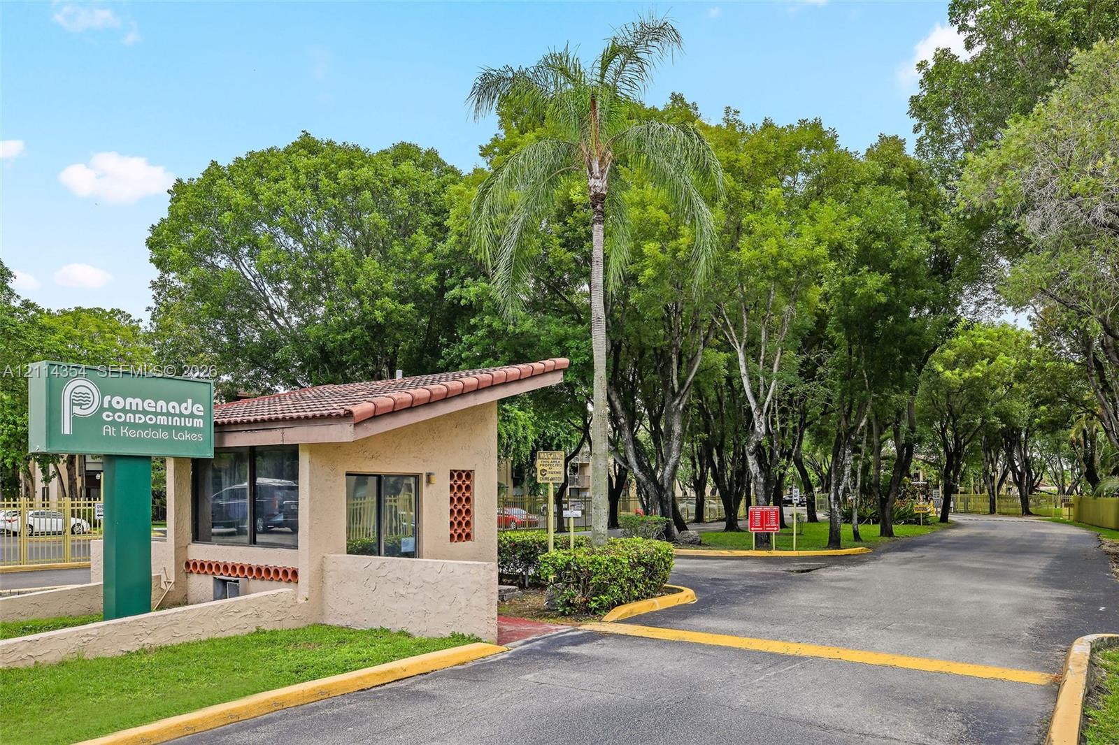 Gated entrance featuring a tile-roofed guardhouse, paved thoroughfare, and mature landscape elements