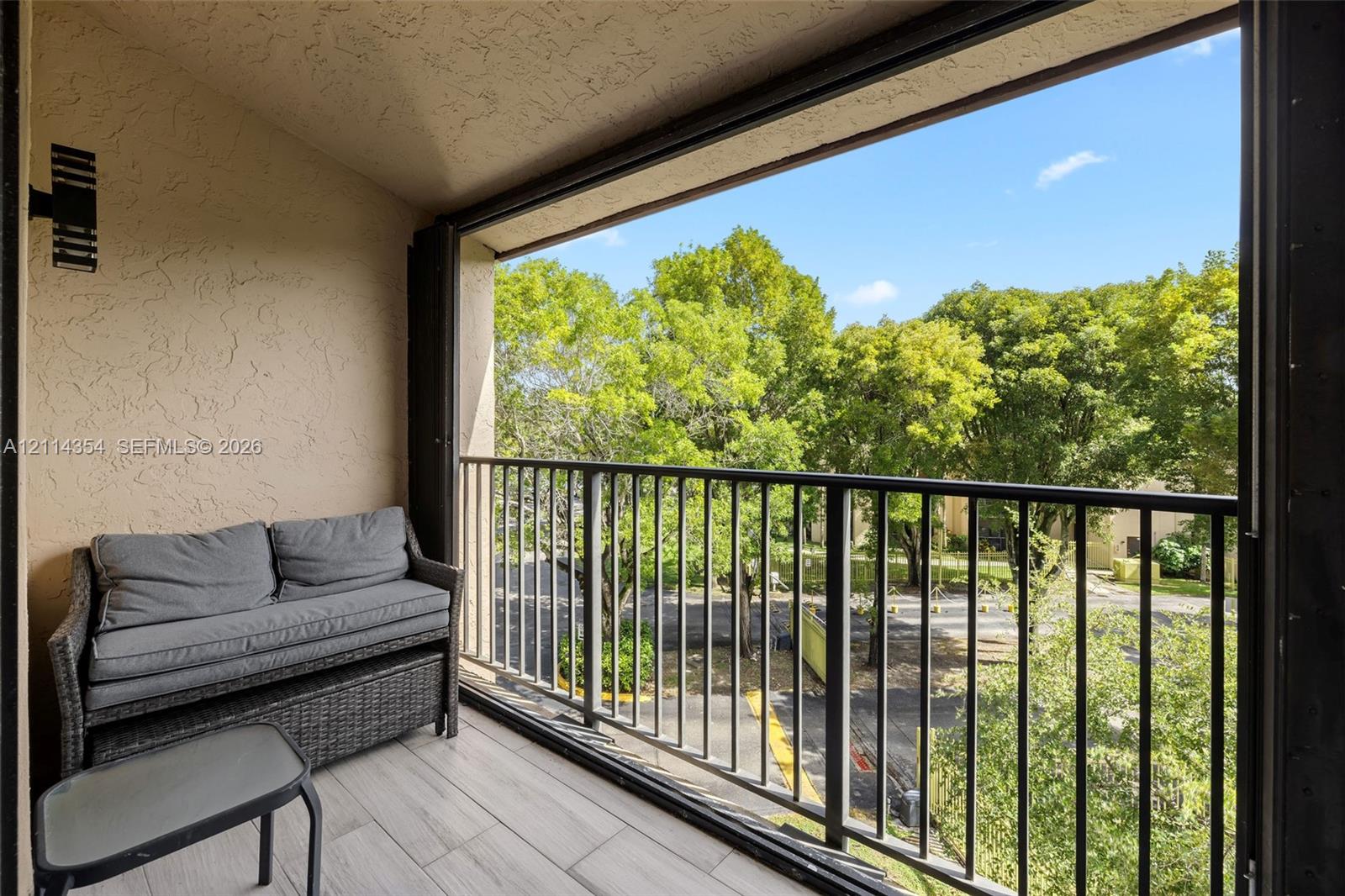 Covered balcony featuring wood-finish tile flooring, textured wall surfaces, black metal railings, and wall-mounted exterior lighting