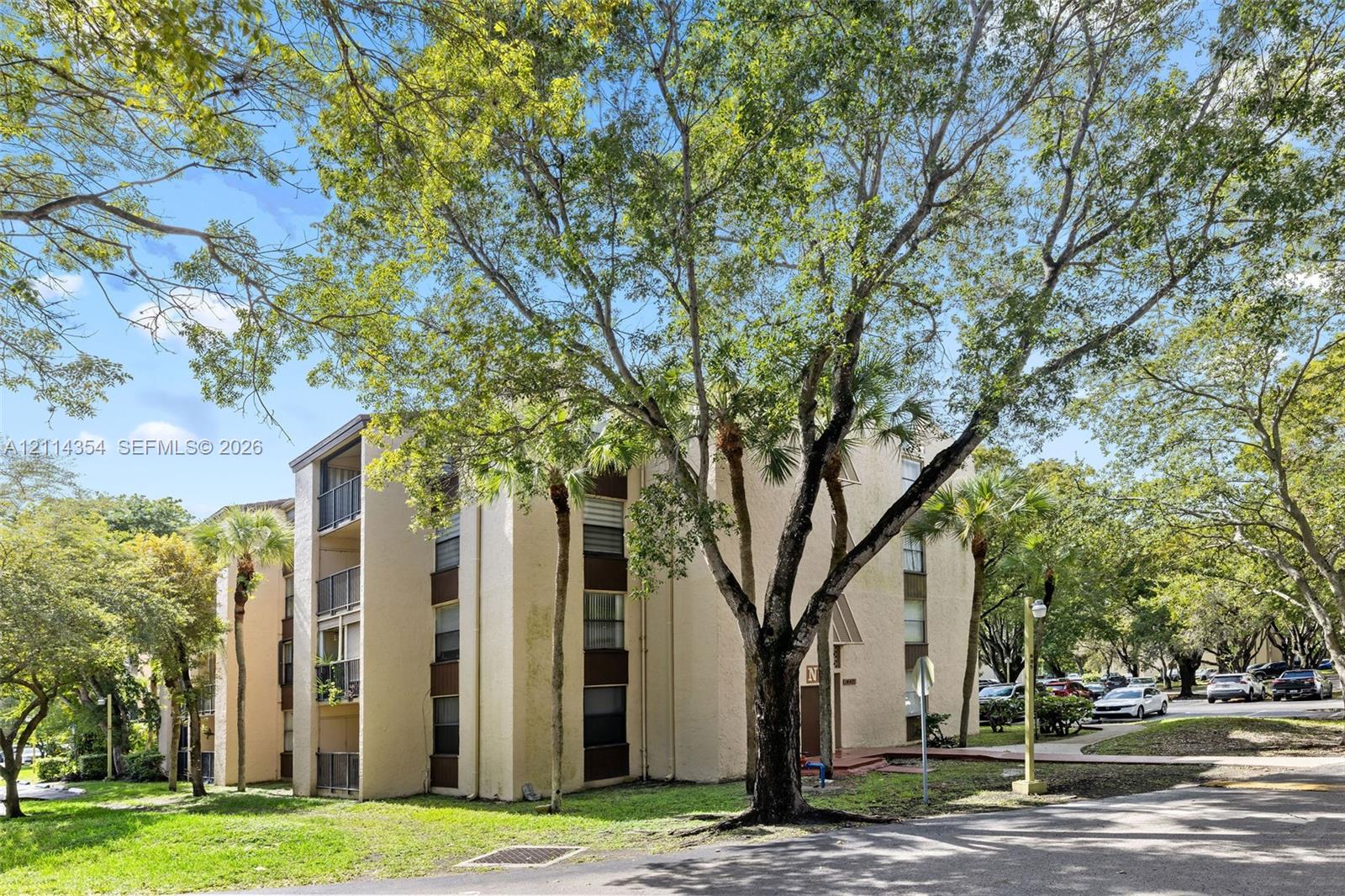 Multi-story exterior featuring a stucco facade, private balconies with metal railings, and mature landscaping