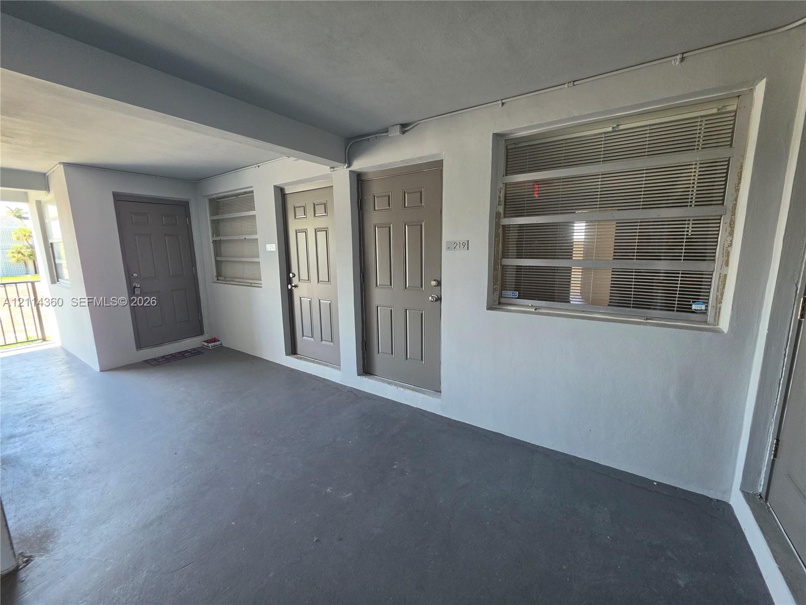 Covered exterior walkway featuring painted concrete flooring, recessed lighting, and multiple paneled entry doors with integrated hardware Covered exterior walkway featuring painted concrete flooring, recessed lighting, and multiple paneled entry doors with integrated hardware