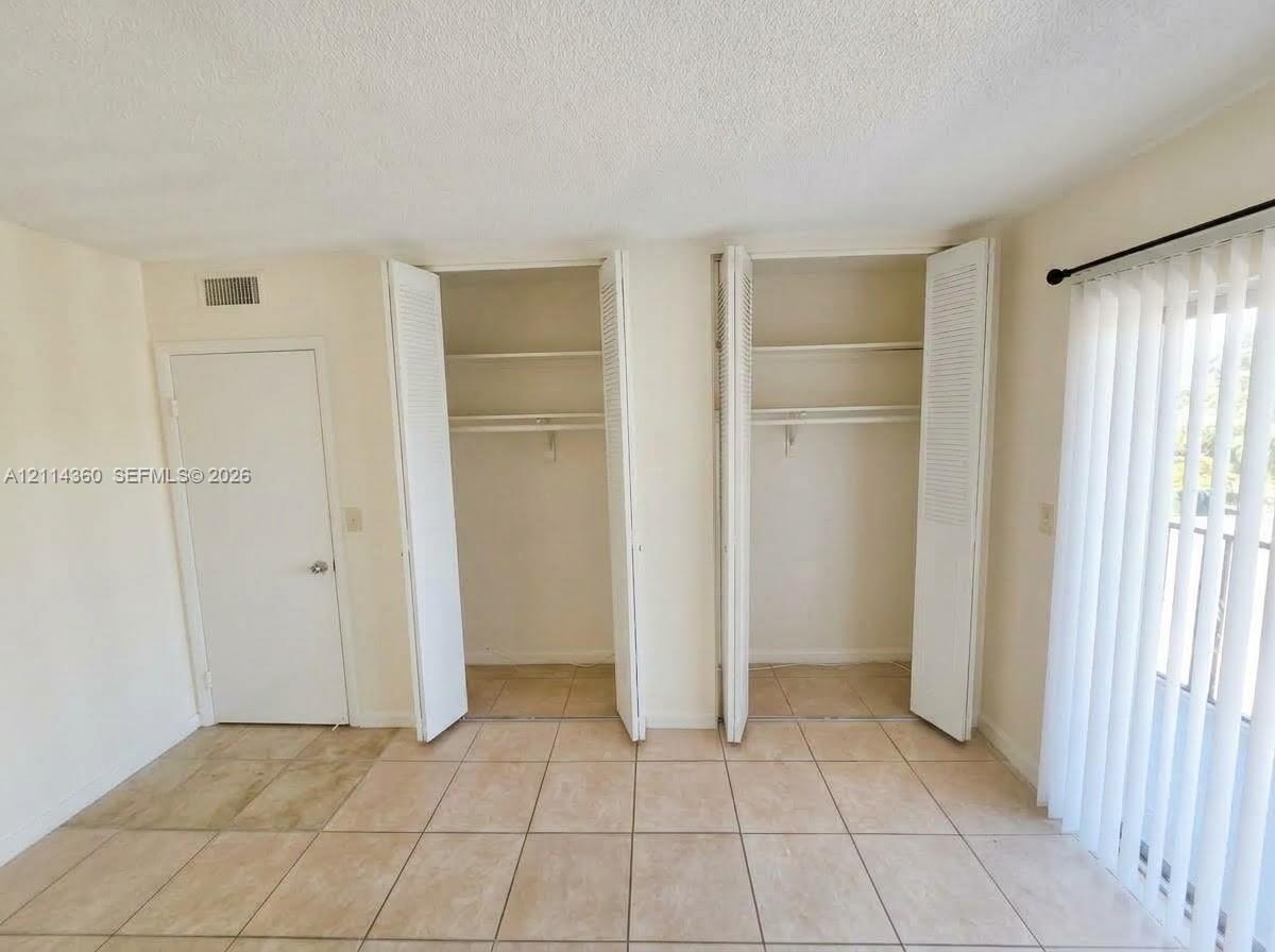 Dual closets with louvered bi-fold doors and interior shelving, tile flooring, and vertical blind window treatments Dual closets with louvered bi-fold doors and interior shelving, tile flooring, and vertical blind window treatments