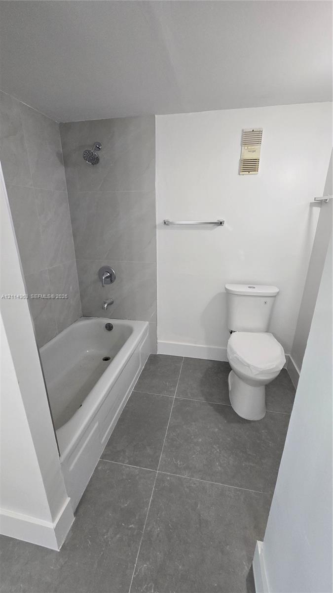 Full bathroom featuring large-format grey tile flooring, a bathtub with a matching grey tile surround, and a wall-mounted chrome towel bar